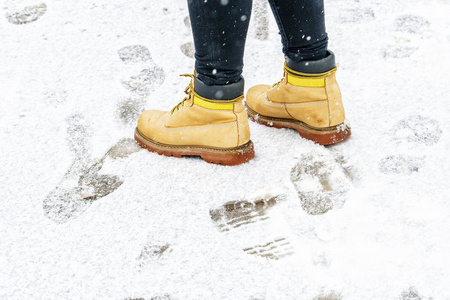 冬天穿黄色皮靴走路。 在一个人的脚上，沿着冰冷的雪路面行走的后景。 冬天在结冰的路上穿一双鞋。 空的，空的，空的冬季天气