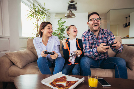 幸福的一家人坐在沙发上玩电子游戏，吃披萨