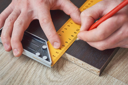 男性用尺子和铅笔测量木板的手