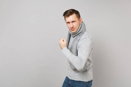 自信的年轻人穿着灰色毛衣围巾，展示二头肌肌肉孤立在灰色背景在工作室。 健康时尚生活方式人真诚情感冷季观念。 模拟复制空间
