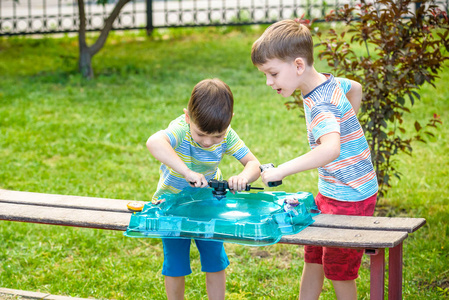 两个男孩在户外玩现代旋转顶部。 儿童娱乐游戏。 由触发器触发的顶部。 在竞技场或战场上有锦标赛的孩子。