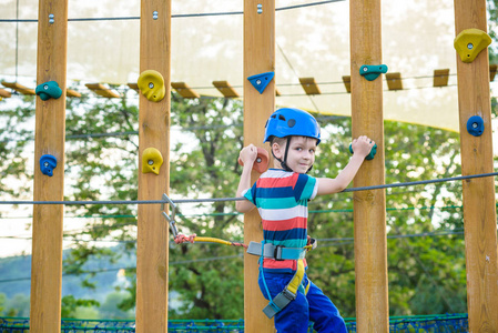 男孩在冒险公园玩得很开心。 蹒跚学步的孩子在绳索操场结构中攀爬。 蹒跚学步的孩子在绳索操场结构中攀爬。 带头盔和的安全攀岩
