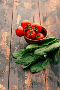 新鲜的菠菜和成熟的西红柿放在木制背景蔬菜的陶土碗里，用于沙拉素食排毒