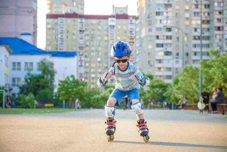 夏天在公园里骑着压路机的小男孩。 快乐的孩子在头盔中学习滑冰。