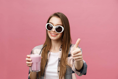 一个可爱的休闲女孩的肖像, 从一个杯子喝橙汁, 看着相机孤立在粉红色的背景
