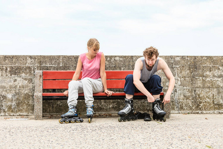 年轻人朋友在户外穿上溜冰鞋。 女人和男人在长凳上。