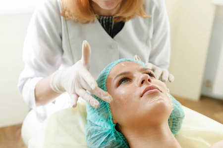 美容师在一家美容院对一位年轻美女的面部皮肤进行超声波去皮术照片