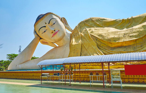绕着大的倾斜的佛陀形象走在MyathaLyaung佛寺周围，周围是郁郁葱葱的花园巴戈缅甸。