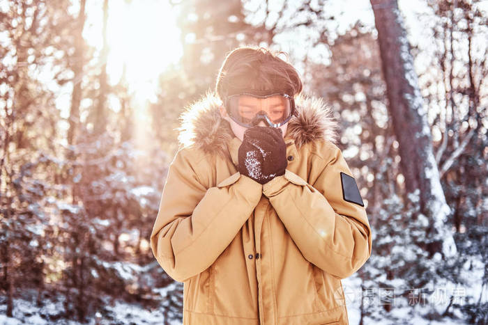 年轻的滑雪者穿着暖和的衣服, 戴着护目镜, 站在雪堆里温暖着双手