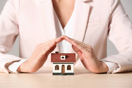 女性代理覆盖房子模型在桌子特写。 家庭保险