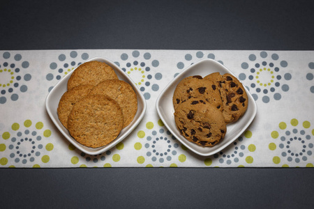 白色碗里有两种不同种类的饼干燕麦片和巧克力饼干。 顶部视图平躺背景。