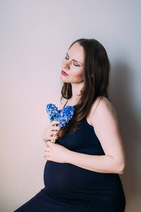 孕妇，闭着眼睛，穿着深蓝色的裙子，坐着一束鲜花