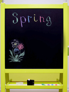 黑色学生粉笔板，有粉笔和多种颜色的铭文春天和油漆花的立场。