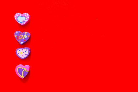 使用爱情粉红色和紫色橡皮擦符号情人节的概念。 学校教育卡。 彩色心擦玩具顶部视图隔离在红纸颜色背景与横幅干净的复制空间。