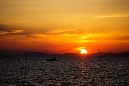 大海上美丽明亮的日落。 夕阳背景下一艘孤独的船和游艇漂流。