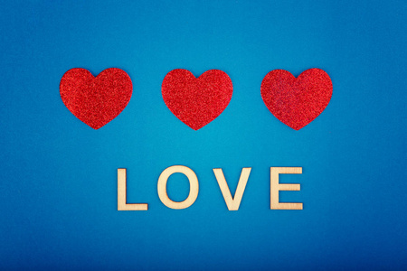 情人节快乐。漂亮的卡片壁纸，中间有三颗红色的心，蓝色的背景和木制的话说爱。一夫多妻制关系和二月假期的概念。