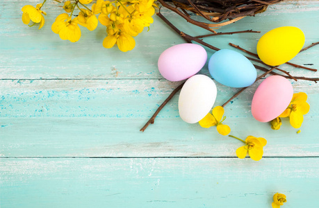 五颜六色的复活节彩蛋在巢与花在乡村木制木板背景在蓝色油漆。 春天的假期。 老式彩色色调风格。 俯视构图。