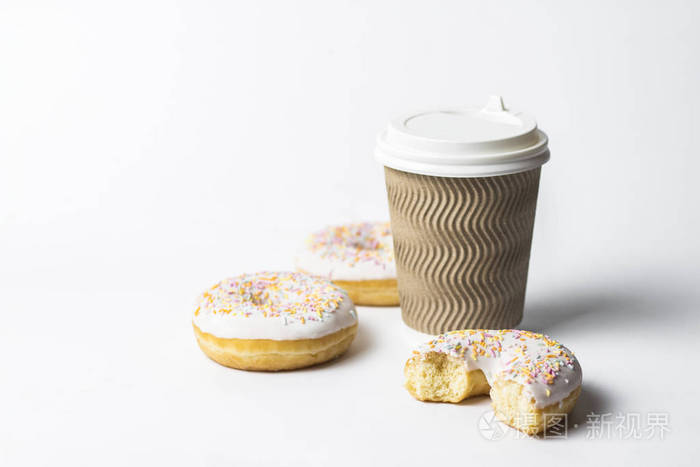 一个纸杯，有盖子咖啡或茶，新鲜美味的甜甜圈和甜的多色装饰糖果在白色的背景。 面包店概念新鲜糕点美味早餐快餐