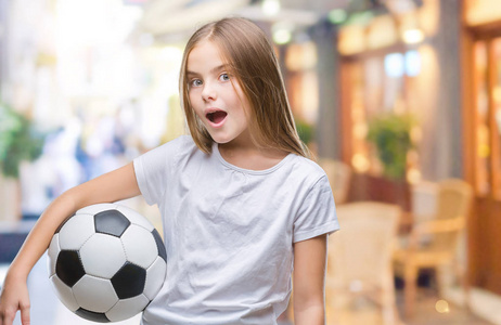 年轻漂亮的女孩抱着足球球在孤立的背景下被吓得满脸惊讶恐惧和兴奋