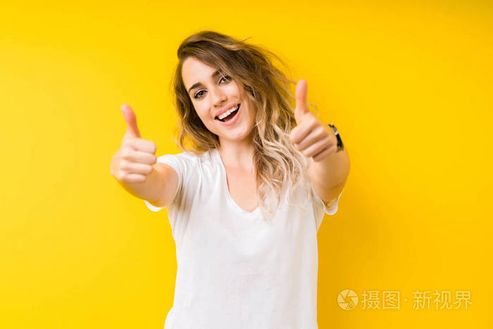 年轻漂亮的金发女人在黄色的背景上赞成做积极的手势,用手竖起大拇指