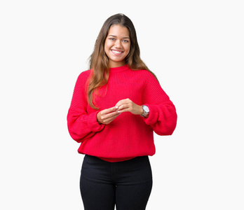 年轻漂亮的黑发女人穿着红色的冬季毛衣，双手分开，手指交叉微笑，轻松愉快。 成功和乐观