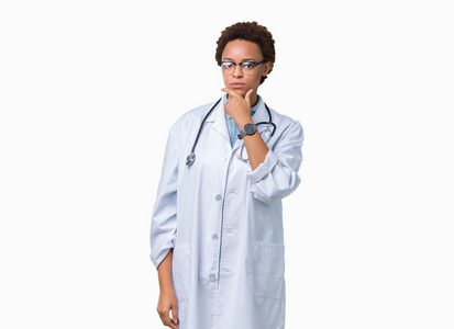 年轻的非裔美国医生女士穿着医用外套，在孤立的背景下，自信地看着相机，微笑着交叉的手臂和举起的手在下巴上。 积极思考。