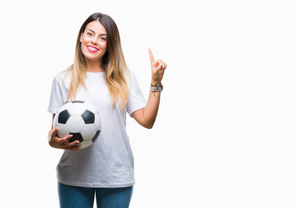 年轻漂亮的女人抱着足球在孤立的背景下惊讶的想法或问题，手指和快乐的脸第一