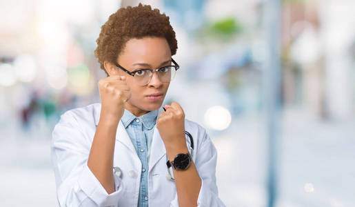 年轻的非裔美国医生女士穿着医用外套，背景偏僻，准备用拳头防御手势，愤怒和沮丧的脸，害怕问题