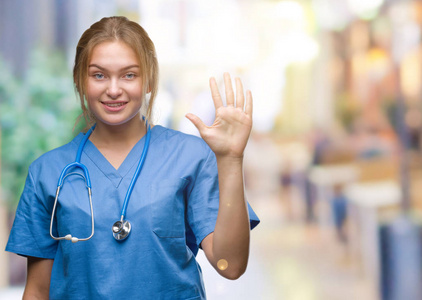 年轻的白种人医生女士穿着外科医生制服，在孤立的背景上显示和举着手指第五，同时微笑自信和快乐。