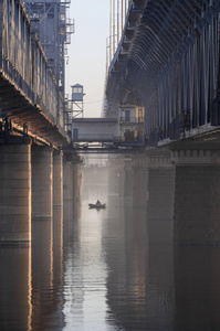 日出时，一个渔夫在河中央桥下的船上。 桥墩之间的渔夫。