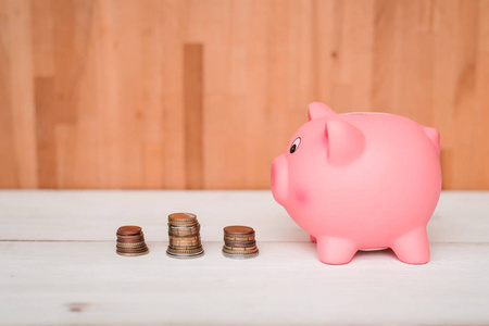 小可爱的粉红色猪储蓄罐在一张木桌上。 三堆硬币，美分和纸币。 储蓄和金融。