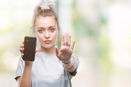 年轻的金发女性，用张开的手在孤立的背景上显示智能手机屏幕，用严肃和自信的表情防御手势做停止标志