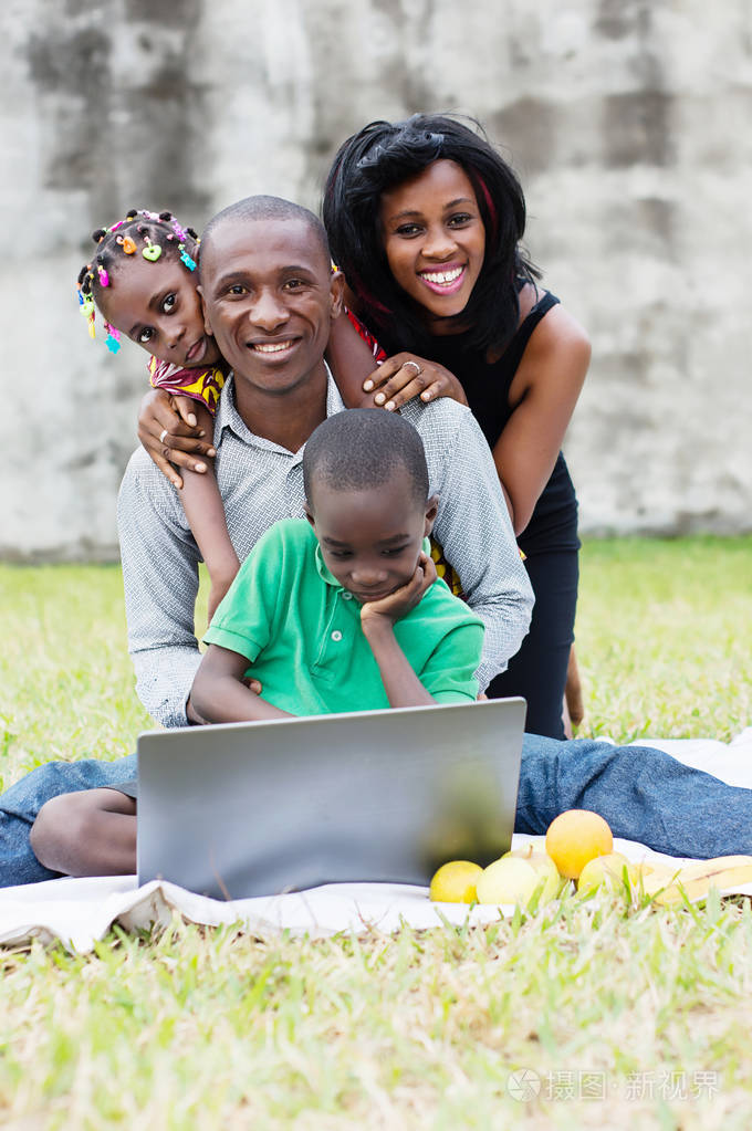 幸福的一家人坐在电脑前的公园里，成群结队地玩耍