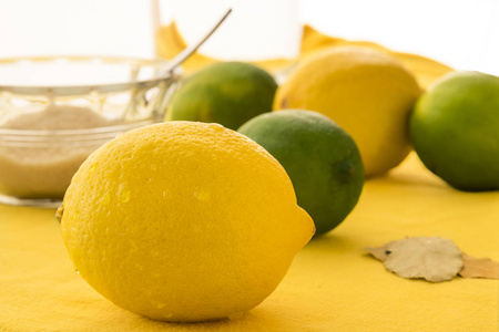 一整个柠檬被隔离在更新鲜的水果和一小碗糖面前。 水果都放在黄色的桌面上，背景是白色的。