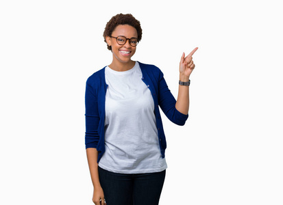年轻美丽的非裔美国妇女戴着眼镜，在孤立的背景上，脸上挂着一个大大的微笑，用手和手指指向一边，看着相机。