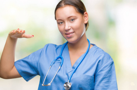 年轻的白种人医生女士穿着医疗制服，在孤立的背景上做手势，双手显示大尺寸的标志符号。 微笑着看着相机。 测量概念。