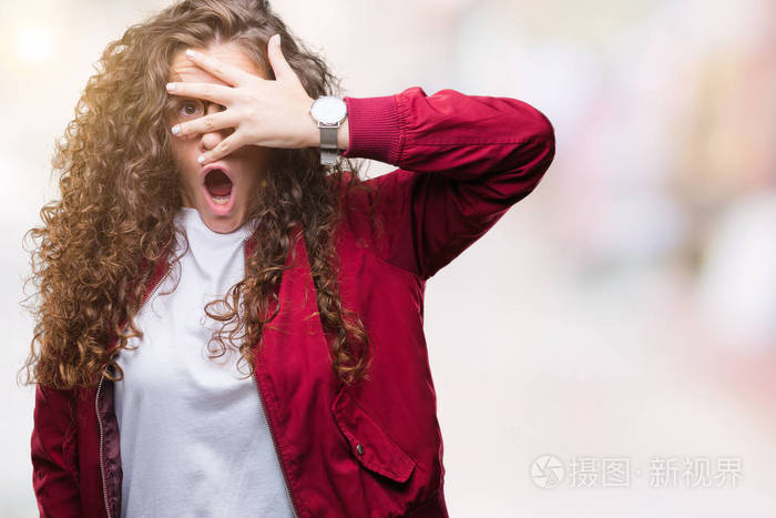 美丽的黑发卷发年轻女孩穿着夹克和眼镜在孤立的背景上偷看震惊覆盖着