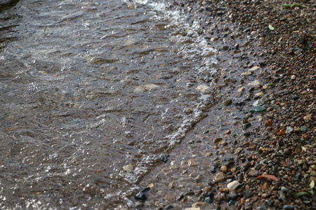 海洋卵石和波浪。 清澈的水近岸，底部有鹅卵石。 海浪拍打在海岸上，流过海岸卵石之上。