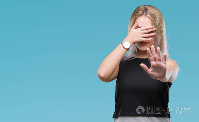 年轻的金发女人在孤立的背景上用手遮住眼睛,用悲伤和恐惧的表情做