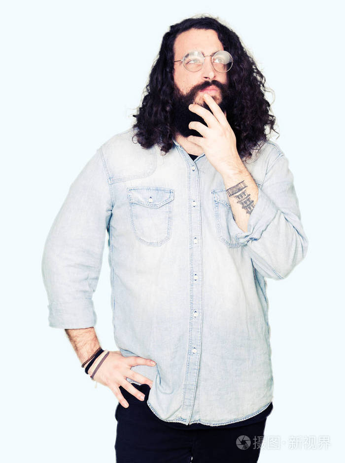 年轻的嬉皮士留着长发和胡须戴着眼镜手放在下巴上想着问题的表情带着