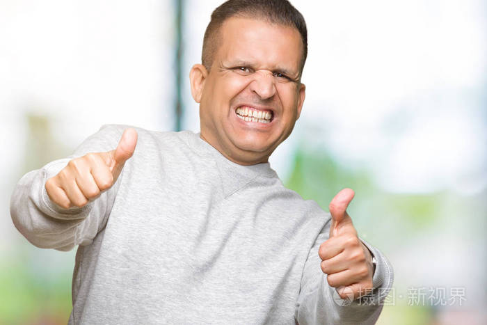 中年阿拉伯男人穿着运动运动衫,在孤立的背景下,批准用手竖起大拇指做