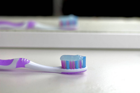 浴室白色架子上的粉红色牙刷反射在镜子里，早上护理牙齿和健康