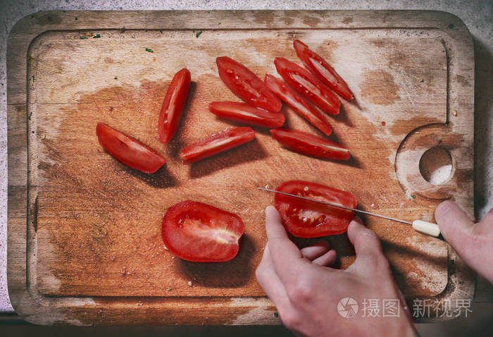 人手拿刀切切片红西红柿在又旧又脏的厨房切割板上准备沙拉顶景特写