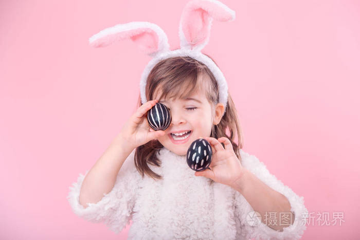 一个可爱的小女孩的肖像，小兔子耳朵和复活节鸡蛋分离在粉红色的背景上