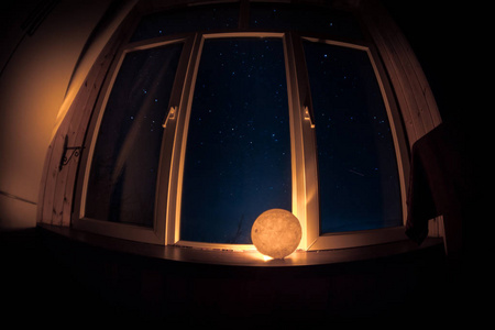 从黑暗的房间透过窗户看到星星的夜景。夜空在黑暗的房间里，用古老的老式灯笼从窗口观看。长期暴露