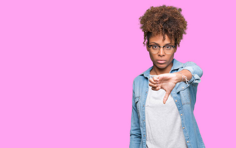 美丽的年轻非洲裔美国妇女戴着眼镜，在孤立的背景上看起来不高兴和愤怒，表现出拒绝和消极的拇指向下的手势。 不好的表情。