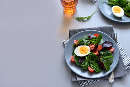 沙拉与菠菜砂仁混合，在灰色的木制背景上留下西红柿和鸡蛋。 素食概念。 选择性聚焦。