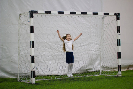 孩子们在室内踢足球。一个兴奋的小女孩站在足球球门上