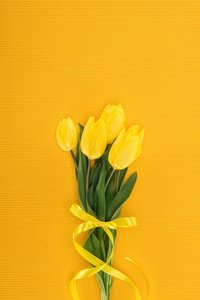 黄色郁金香花束的顶部视图，橙色背景上有丝带