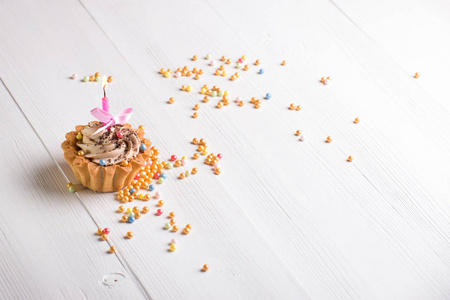 美味的纸杯蛋糕，奶油和蜡烛站在白色的木制背景和彩色糖果。